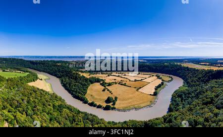 Winding fließender Fluss durch ein ländliches Tal, umgeben von dichtem grünen Wald und trockenen landwirtschaftlichen Weiden unter heller Sonne, Hochwinkel-Panorama Stockfoto