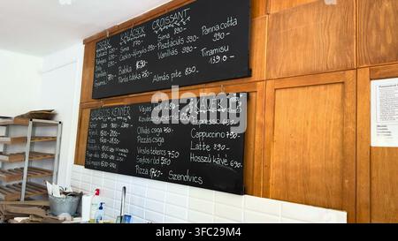 BALATONBOGLÁR, UNGARN - 15. JUNI 2026: Eine Kreidetafel auf einer Holzwand listet Preise für Brot, Gebäck und Kaffee in einer ungarischen Bäckerei in Ba auf Stockfoto