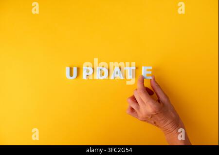Update-Konzept mit einer menschlichen Hand, die UPDATE-Buchstaben auf einem gelben Hintergrund anordnet, mit Kopierplatz. Symbol für die Aktualisierung von Informationen, Software und Systemen Stockfoto