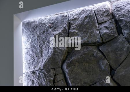 Nahaufnahme einer rauen, unebenen Steinmaueroberfläche, die von weichem seitlich einfallendem Licht beleuchtet wird, wodurch ihre raue Textur und tiefe Spalten betont werden Stockfoto
