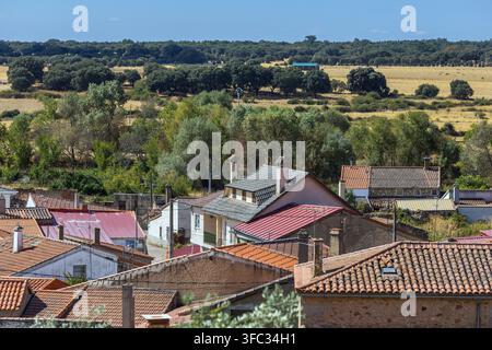 Eine Hochwinkelaufnahme zeigt ein ruhiges spanisches Dorf mit Ziegeldächern, das sich unter weitläufigen, sanften Feldern und grünen Wäldern unter einem klaren blauen Himmel befindet Stockfoto