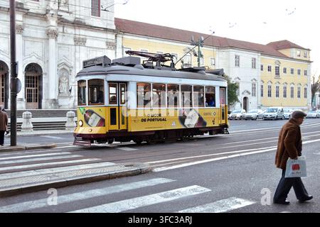 Merida, 17. Dezember 2017; Gelbe Straßenbahn passiert eine historische Kirche und ein Mann überquert eine Straße in Lissabon. Stockfoto