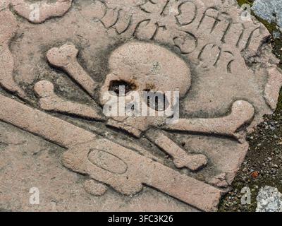 WISMAR, DEUTSCHLAND, 30. MÄRZ 2026: Eine antike Steintombplatte mit einer Gravur, die einen Schädel und ein Kruzifix als Memento-mori-Symbol mit historischer deutscher Schrift darstellt Stockfoto