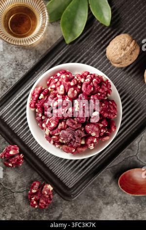 Schüssel mit roten Walnusskernen auf einem dunklen Tablett mit Tee und ganzen Walnüssen. Stockfoto