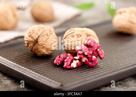 Ganze Walnüsse und rote Walnusskerne auf einem dunklen Holzbrett als Hintergrund. Stockfoto