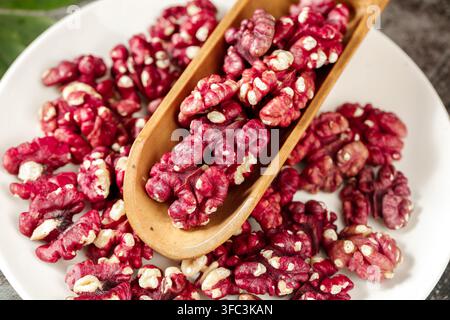 Rot überzogene Walnusskerne auf einem weißen Teller mit einer hölzernen Schaufel. Stockfoto