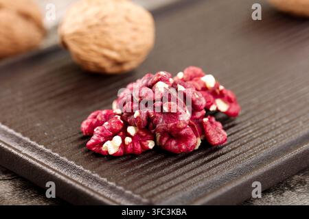 Rote Walnusskerne auf einem dunklen Holzbrett mit ganzen Walnüssen im Hintergrund. Stockfoto