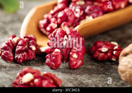 Rote Walnusskerne mit einer hölzernen Schöpfkelle auf einer grauen Steinfläche. Stockfoto
