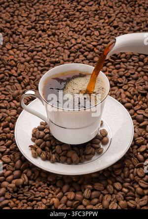Ansicht von Kaffee, der in eine weiße Porzellantasse gegossen wird, umgeben von gerösteten Kaffeebohnen in Islamabad, Islamabad Capital Ter., Pakistan. Stockfoto