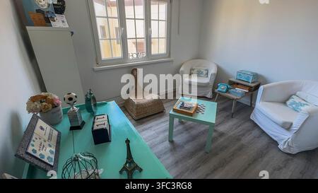 Corvo, Azoren, Portugal Gemütliches, helles Wohnzimmer mit hellen Möbeln. Weiche weiße Stühle stehen in der Nähe eines Fensters mit Holzrahmen. Mintgrüne Koffern Stockfoto