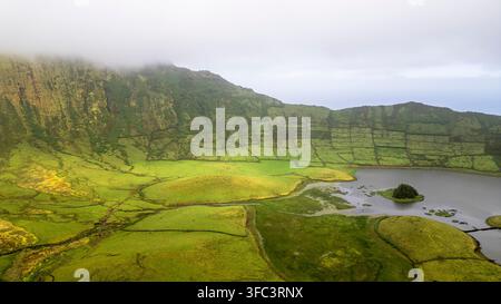 Corvo, Azoren, Portugal Luftaufnahme der üppigen grünen Terrassen der Insel Corvo, die einen ruhigen See umgeben. Nebel zieht über die zerklüfteten Hügel und mildert das Land Stockfoto