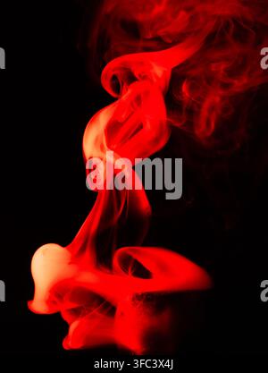 Lebendiger roter Rauch wirbelt anmutig vor einem dunklen schwarzen Hintergrund. Stockfoto