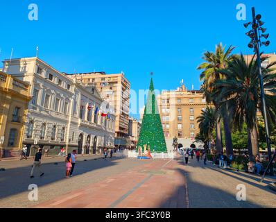 SANTIAGO, CHILE - 03. DEZEMBER 2025: Ein hoher geschmückter Weihnachtsbaum steht auf dem Plaza de Armas-Platz, umgeben von historischen Gebäuden und Palmen in San Stockfoto