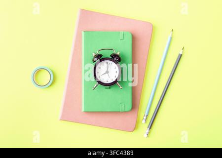 Bunte Schreibwaren mit einer Uhr, Notizbüchern und Bleistiften auf einem hellen gelben Hintergrund, die ein fröhliches Konzept für Zeitmanagement, Studium schaffen, Stockfoto