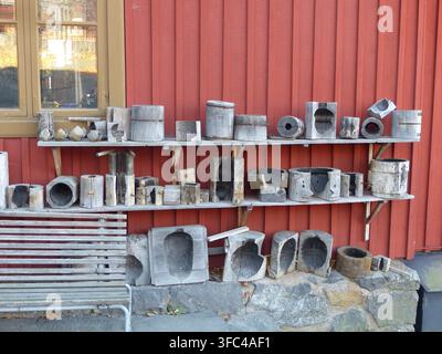 Reihen rustikaler, verwitterter Holzherstellungsformen, die auf Außenschränken entlang einer traditionell rot gestrichenen Wand organisiert sind. Stockfoto