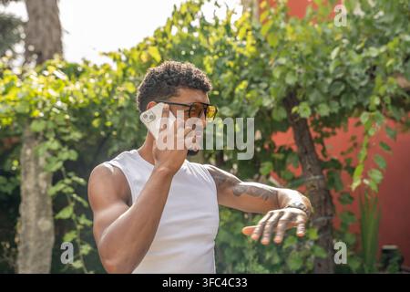 Junger Mann mit lockigem Haar und Brille spricht im Freien am Smartphone Stockfoto