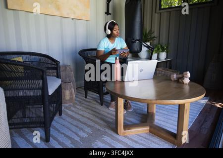Erwachsene afroamerikanische Frau verwendet Laptop und Telefon mit Kopfhörern in der Nähe eines Mikrofons im Studio, Kopierraum Stockfoto