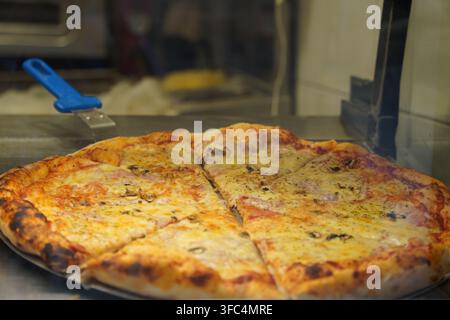 Frisch gebackene Pizza mit geschmolzenem Käse und Belägen in Dreiecke geschnitten Stockfoto