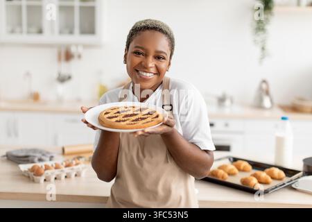 Zufriedene schwarze Frau hält frisch gebackenes Dessert in der Küche, Kochkonzept Stockfoto