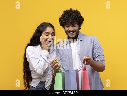 Glücklicher südasiatischer junger Mann und Frau, die gemeinsam beim Einkaufen Spaß haben, gelber Hintergrund Stockfoto
