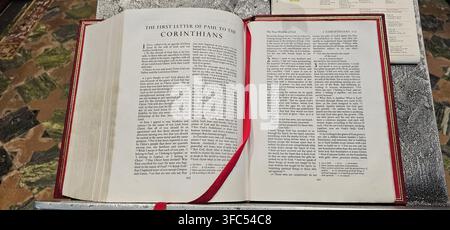 Offene Bibel, die den ersten Brief des Paulus an die Korinther zeigt, von oben auf einem Kirchenpult oder einer Lesearmatur betrachtet, mit einem roten Leseband als Lesezeichen Stockfoto