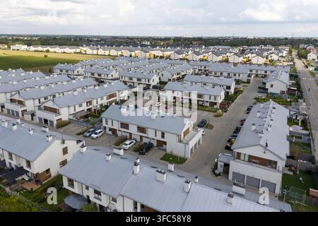 Luftbild einer modernen Vorstadt-Siedlung mit Reihen von weißen Häusern mit grauen Metalldächern, gepflasterten Einfahrten und grünen Rasenflächen in Polen. Stockfoto