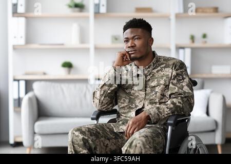 Nachdenklicher schwarzer Mann im Rollstuhl in Militäruniform, Büroumgebung. Gesundheitskonzept Stockfoto