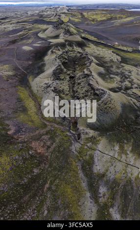 Drohnenperspektive einer moosbedeckten vulkanischen Bergrückenformation, umgeben von dunklen Lavafeldern und Tundravegetation im Süden Islands. Stockfoto
