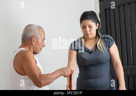 Junge Frau hilft einem älteren Mann mit einem Stock aufzustehen und zeigt Fürsorge und Mobilitätsunterstützung Stockfoto