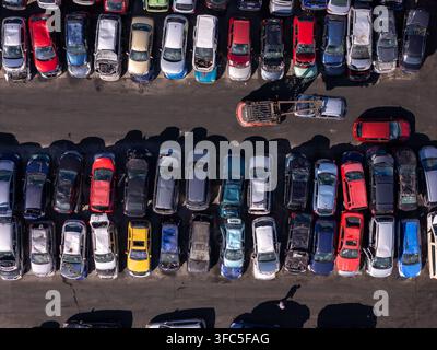 Luftbild eines Autoverwerterhofs mit Reihen von zerstörten und beschädigten Fahrzeugen in verschiedenen Farben, wobei ein Gabelstapler in der Mitte ein Auto manövriert, i Stockfoto