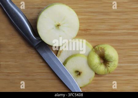 Nahaufnahme einer Granny-Smith-Apfel (Malus domestica), halb geschnitten, mit einem silbernen Messer daneben. Konzept: Obst, Snack, Hausapfel, Mittagessen, frisch Stockfoto