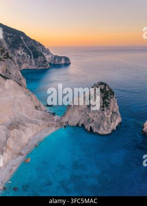 Erleben Sie die atemberaubende Schönheit von Myzithres Beach in Zakynthos, Griechenland, während die Sonne über den ruhigen Gewässern untergeht und ein magisches Licht auf die felsigen Klippen wirft Stockfoto