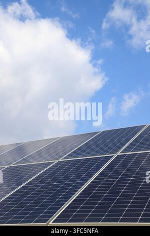 Vor einem klaren blauen Himmel mit weißen Wolken bilden die tiefblauen solarphotovoltaischen Paneele einen auffälligen Kontrast. Die klare Gitterstruktur der Zellen sh Stockfoto