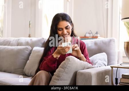 Junge indische Frau sitzt auf einem bequemen Sofa zu Hause Stockfoto