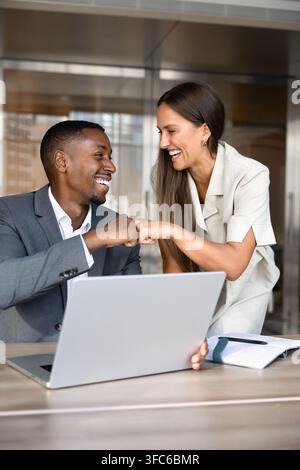 Kollegen teilen einen feierlichen Fauststoß, während sie an einem Laptop zusammenarbeiten Stockfoto