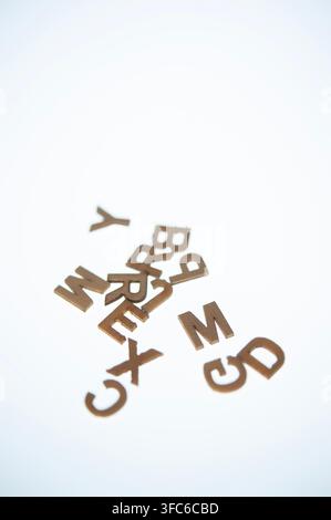 Verstreute hölzerne Alphabetbuchstaben auf einer weißen Oberfläche, ein minimales Konzept für Sprache, Rechtschreibung, Alphabetisierung, Bildung, Kommunikation und Wortspiele Stockfoto
