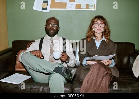 Porträt verschiedener Kollegen, die auf einem Sofa in einem Retro-Büro sitzen Stockfoto