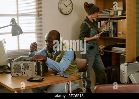 Schwarzer Mann repariert Computer mit Frau, die in einem Retro-Büro arbeitet Stockfoto
