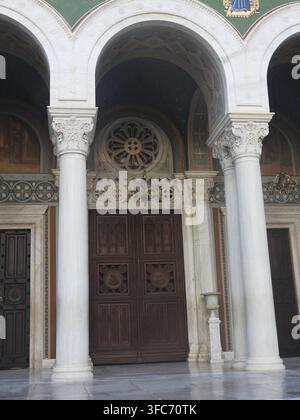 Fassade der Metropolitankathedrale von Athen mit einer großen Holztür, einem aufwendigen Rosettenfenster und dekorativen Marmorsäulen unter Bögen, die darstellen Stockfoto