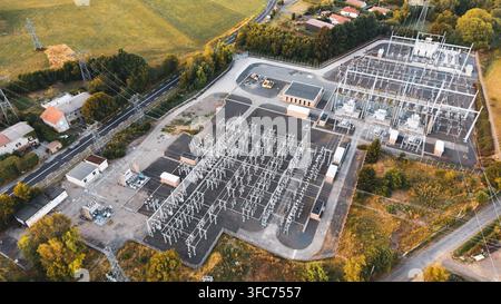 Luftaufnahme eines Umspannwerks mit Metallkonstruktionen, Transformatoren und Stromleitungen, umgeben von Bäumen und ländlichen Straßen in Orcines, Auvergne- Stockfoto