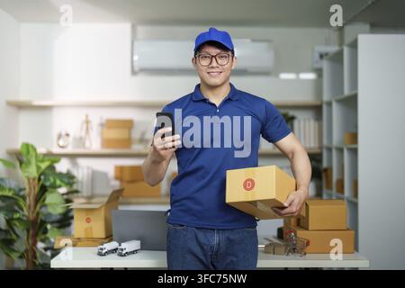 Eine Lieferperson steht in einem Logistikbüro, hält Pakete und ein Smartphone und ist bereit, Kunden zu helfen. Steht für moderne Lieferdienste Stockfoto