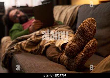 Mann entspannt sich auf dem Sofa und nutzt ein Digitales Tablet zu Hause Stockfoto