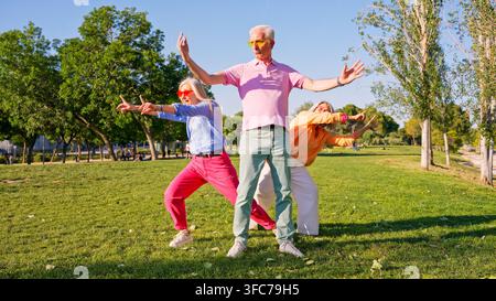 Aktive Seniorenfreunde tanzen im Freien in einem farbenfrohen Park Stockfoto