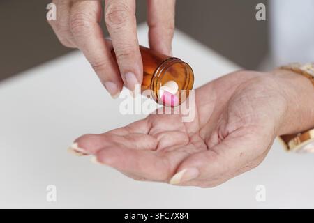 Eine Person gießt rosa Kapseln aus einer Rezeptflasche in ihre Hände und konzentriert sich auf die Medikation Stockfoto