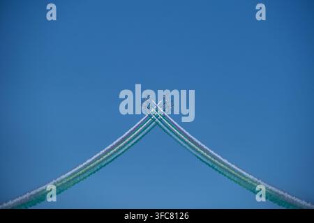 Kampfflugzeuge auf einer Luftshow fliegen in Form einer geometrischen Figur mit bunten, hellen Rauchspuren vor einem blauen Himmel mit Wolken. Luftshow pro Stockfoto