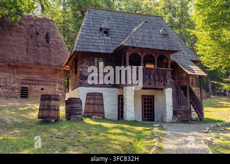 Traditionelles rumänisches Holzhaus mit Verandafässern und steilem Schindeldach im Sonnenlicht Stockfoto