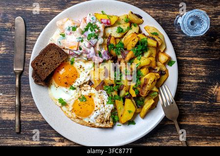 Traditionelles ukrainisches Essen, gebratene Kartoffeln mit Zwiebeln, gebratene Eier, Gemüsesalat, schwarzes Brot und ein Glas Wodka auf Holzuntergrund, Nahaufnahme, zu Stockfoto