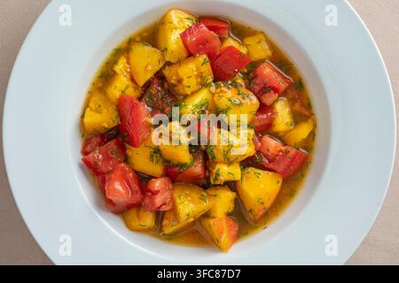 Farbenfroher Sommersalat mit Tomaten und Pfirsich, gewürzt mit einer Sauce aus Olivenöl, Zitronensaft und Balsamico-Essig, Nahaufnahme Stockfoto