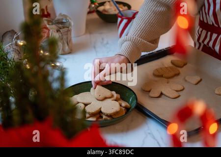 Frau arrangiert frisch gebackene Lebkuchen auf einem Teller während einer gemütlichen Weihnachtsbacksession Stockfoto