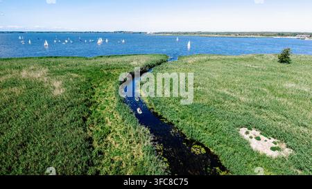 Dronelandschaft eines grünen Sumpfkanals, der zu einem See mit Segelbooten am Horizont führt Stockfoto